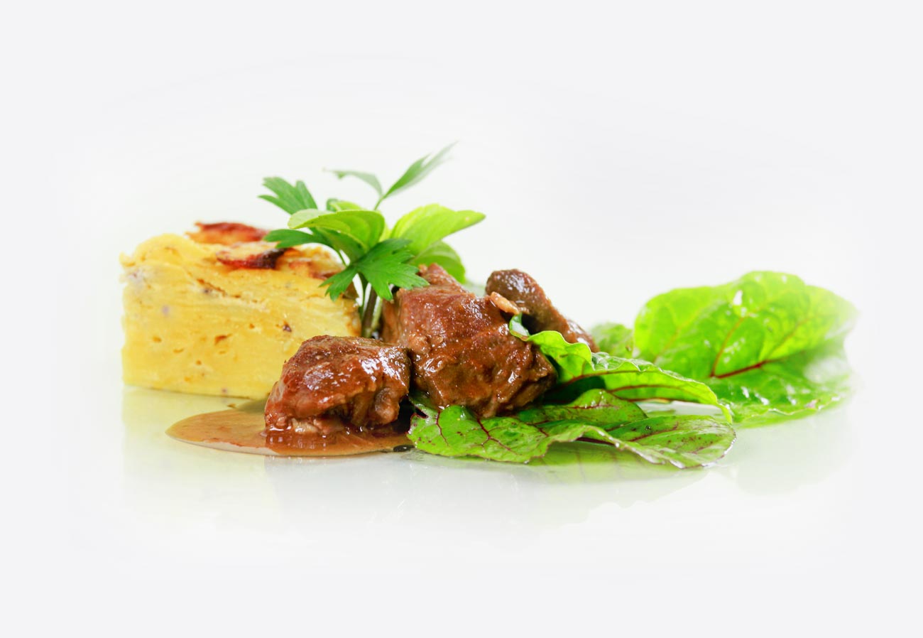 Kartoffelgratin mit schmorfleisch und grünem Salat auf weißem Grund